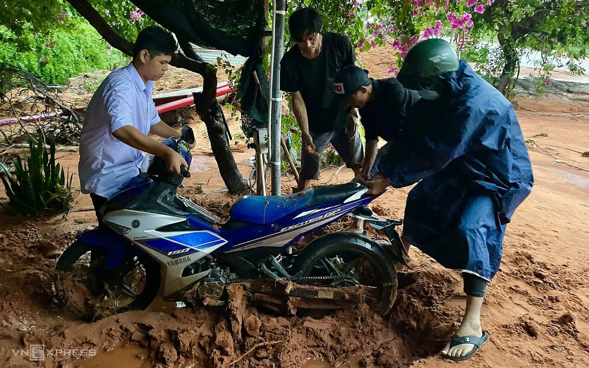 Anh Đức (thứ 2 từ trái qua) cùng một số người kéo xe máy bị cát vùi lấp lên. Ảnh: Việt Quốc