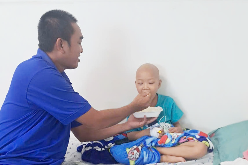 Anh Lợi bón đồ ăn cho con khi đang điều trị tại bệnh viện Nhi đồng Thành phố, hôm 29/8. Ảnh: Hoa Sen
